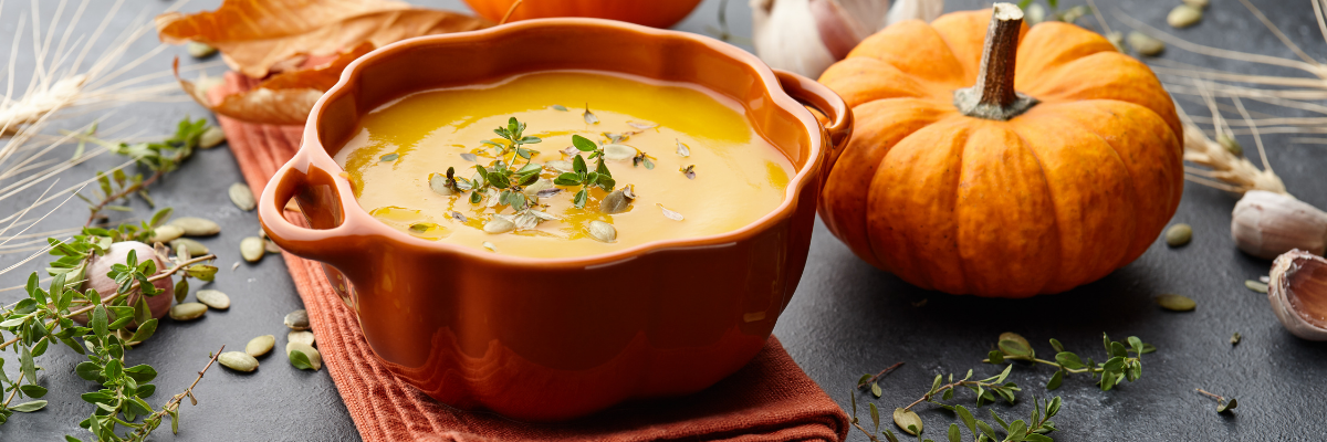 Pumpkin soup in a pumpkin-shaped ceramic bowl with herbs and pumpkins on a dark background