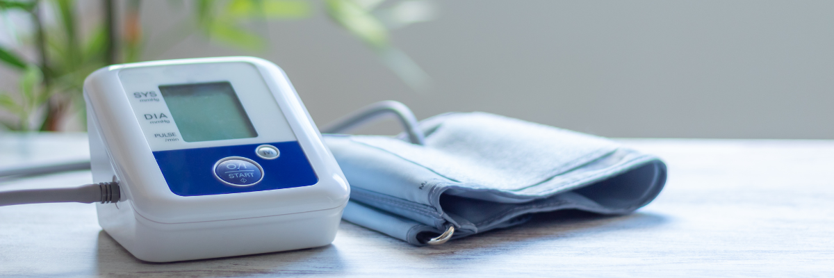 A blood pressure monitor sits on a table with a blurred plant in the background. 