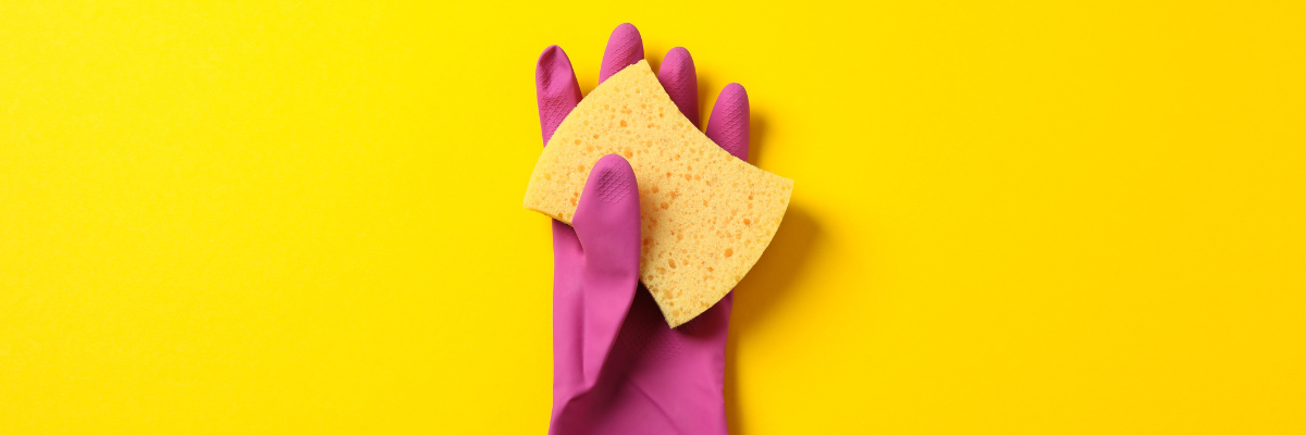 A yellow background with a pink cleaning glove holding a sponge.