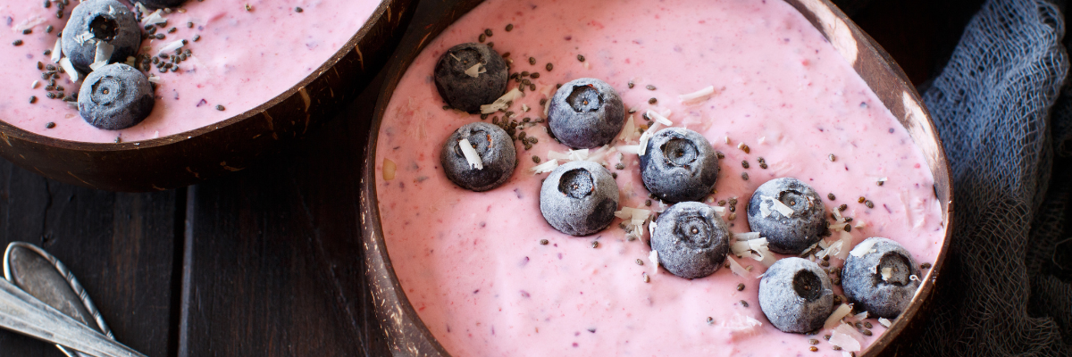 Blueberry coconut smoothie bowls in wooden bowls on a dark wooden surface with silver spoons. 