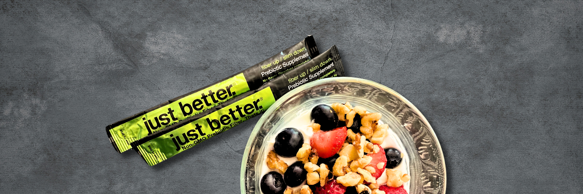 A bowl of yogurt, fruit, and nuts with two stick packs of just better prebiotic fiber.