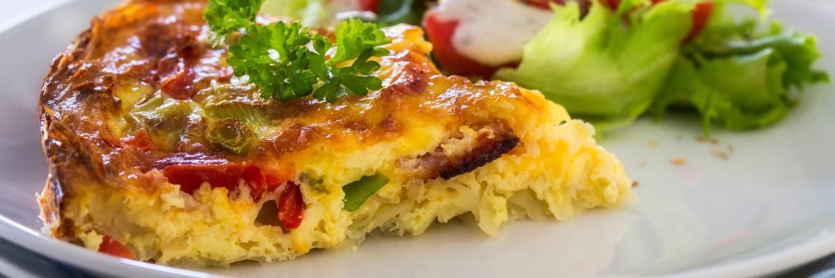 A slice of crustless veggie quiche on a plate with a garden salad.