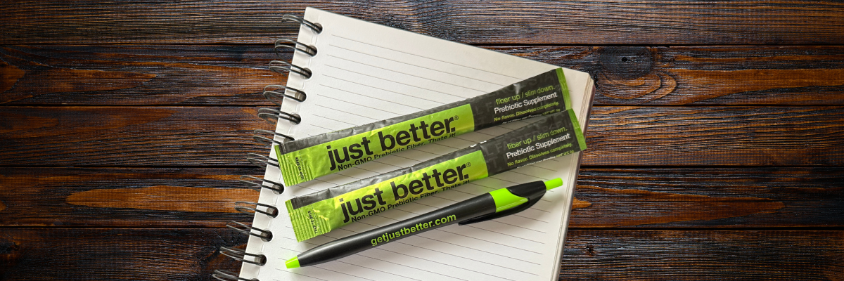A pad of paper with two stick packs of just better fiber and a pen on a dark wooden surface.