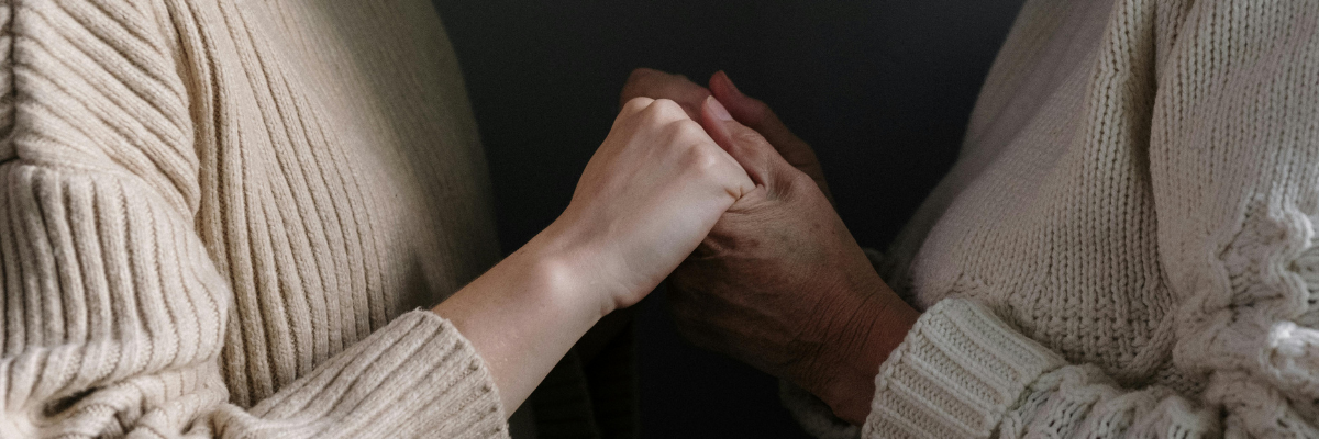 A woman holds hands with an elderly woman. 