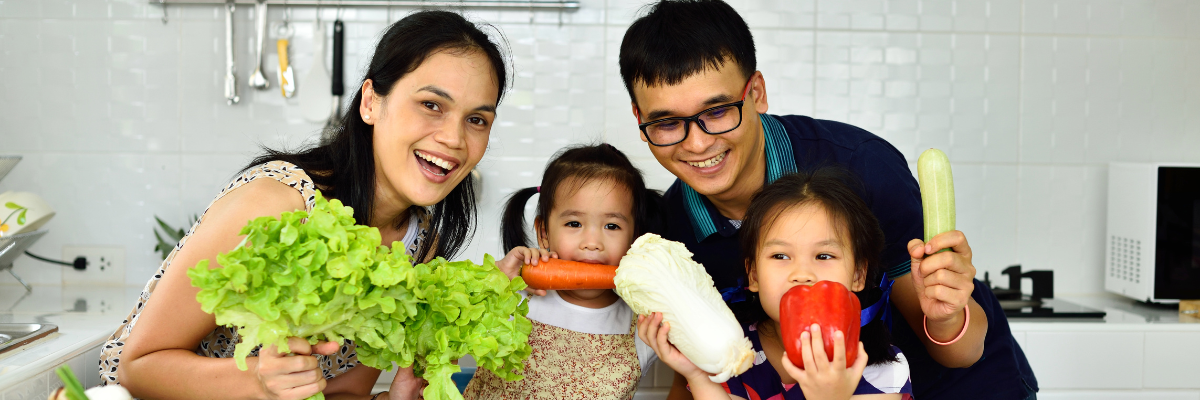 A young family is shown holding various fresh produce items for meal prep. 