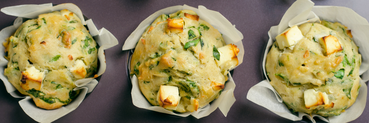 Three feta spinach muffins with paper liners sit on a dark surface.