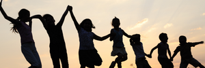 A silhouette of children jumping with a sunny sky in the background. 