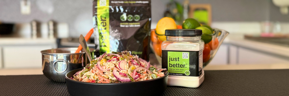 A blurred background of a kitchen. The focus is on a serving dish of Roasted Asparagus Spring Salad with Creamy Lemon-Dill Dressing, with a container of just better prebiotic fiber nearby. 