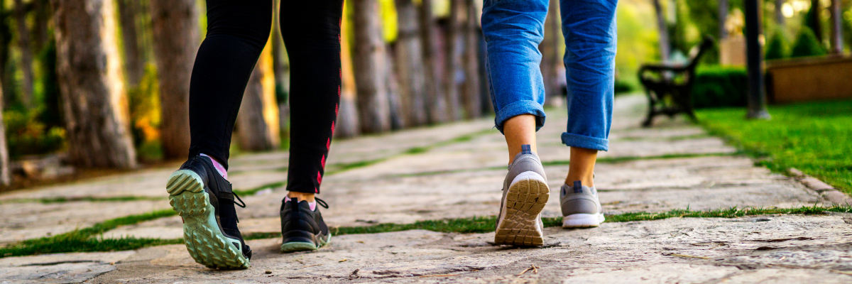 Two people walking down a park path with a closeup of only the lower legs.. 