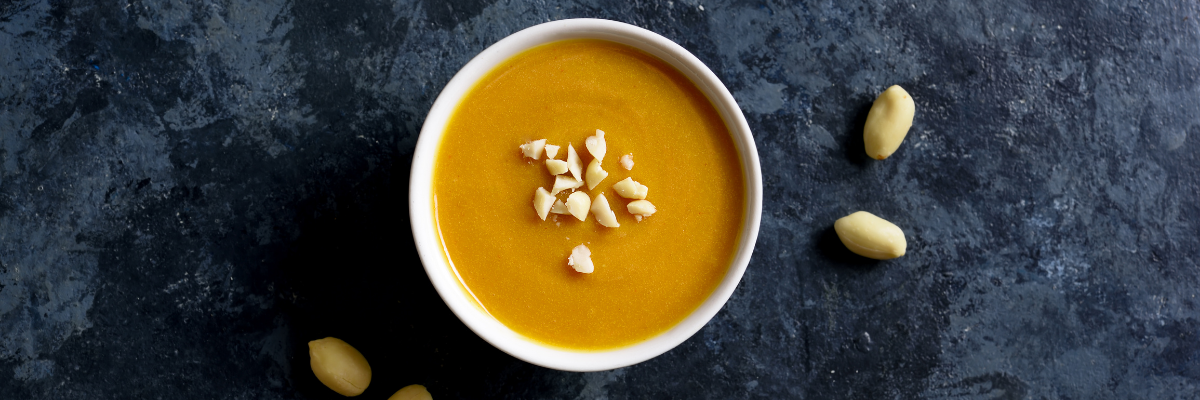 A dark surface with scattered shelled peanuts and a bowl of peanut sauce.