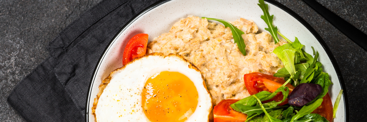 Prebiotic Savory Oats with Eggs + Greens with a dark background with various ingredients scattered.